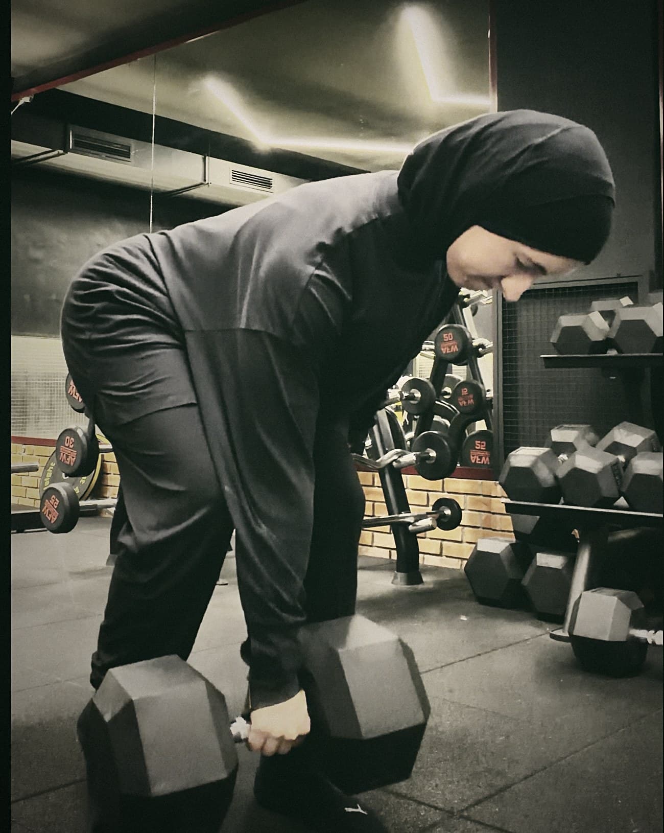 Katia in the gym, bending to pick up a pair of dumbbells.